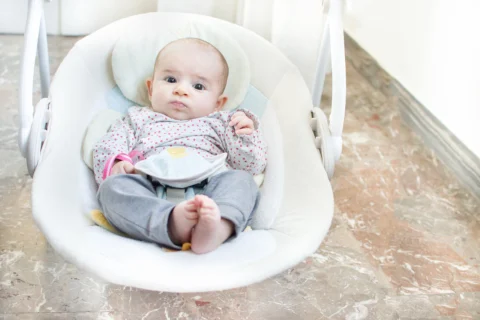 Wide-awake baby resting in a white swing during supervised time