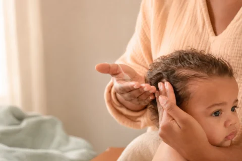 A baby with soft curly hair and visible natural frizz wrapped in a light towel