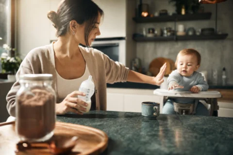 Parent keeps a jar of chocolate malt drink away while holding a prepared baby bottle.