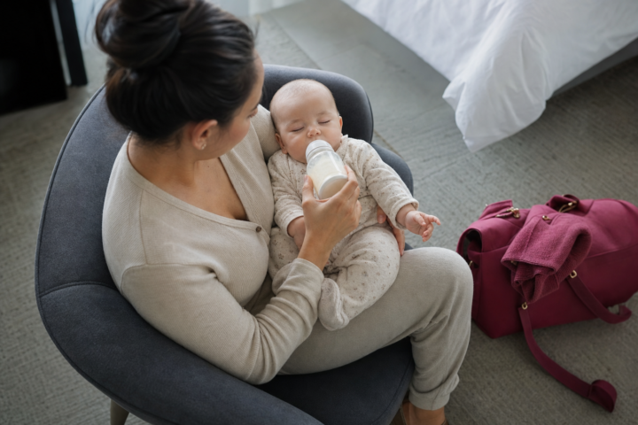 Attentive woman bottle-feeds a drowsy baby in a bright hotel room