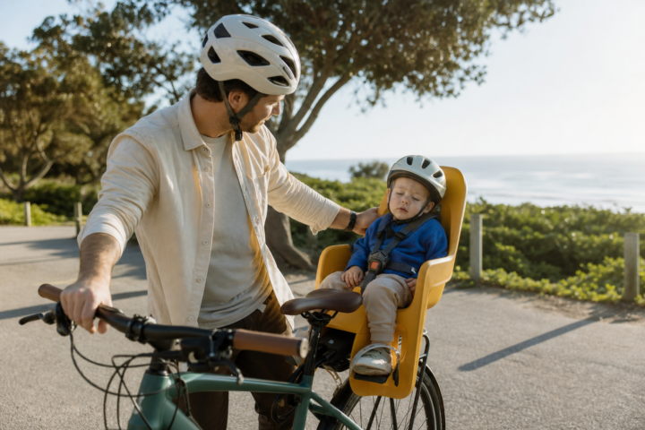 Father checks a drowsy helmeted toddler in a rear bicycle seat