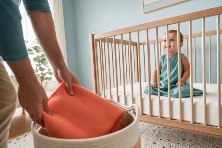 Father stores a coral blanket while an awake baby sits in an empty crib