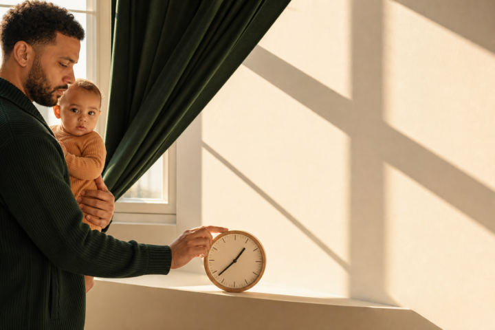 Father holding his baby while adjusting a clock by a sunlit window