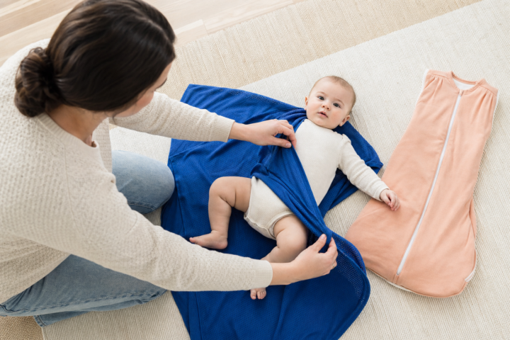 Parent wraps a cobalt swaddle around an awake baby on a family-room play mat