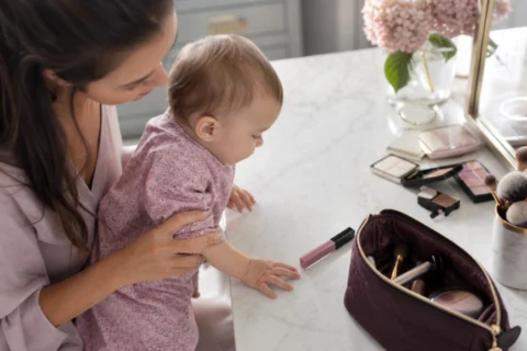 Caregiver gently holding a baby near a vanity with an open makeup bag and a lip gloss tube on the counter.