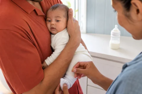 Two caregivers support a drowsy baby upright after feeding