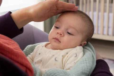Caregiver gently shading the light while looking at a calm baby's faintly veined eyelids