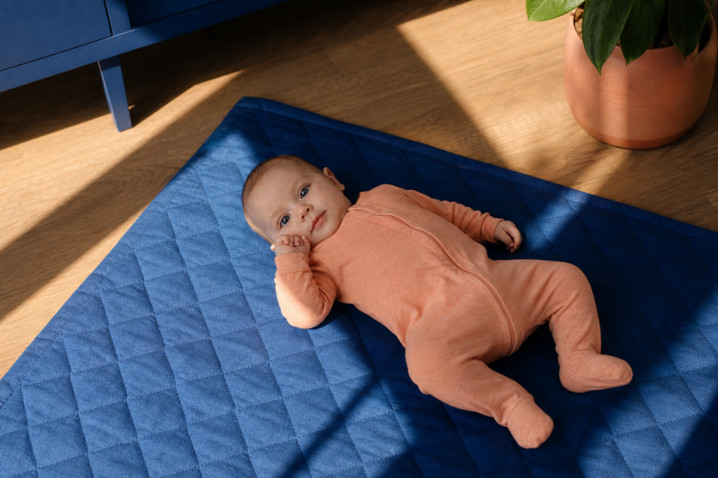 Alert baby lying on a blue play mat in a sunlit family room