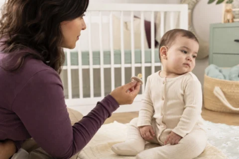 Caregiver offers pacifier to baby who turns away in a bright nursery