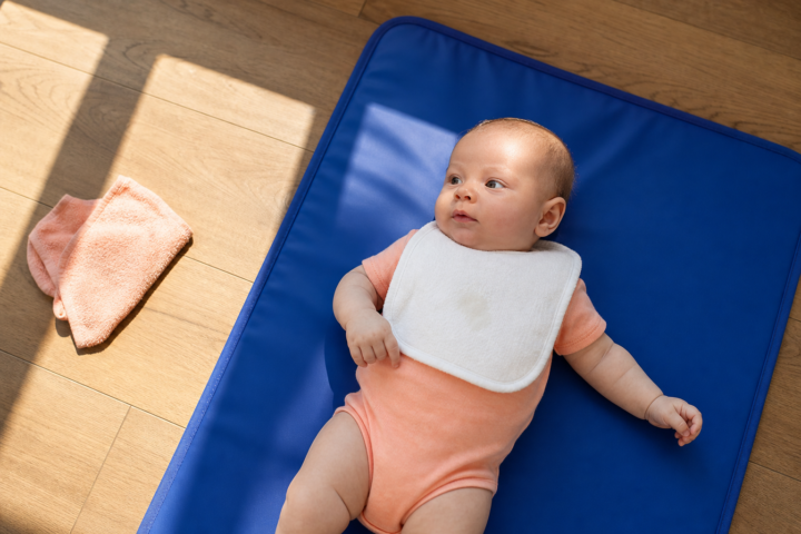 Calm baby on a blue floor mat wearing a white bib