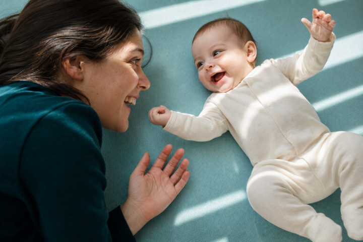Smiling baby reaches toward a parent on a teal play mat