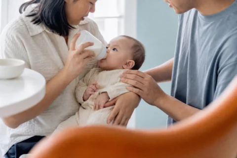 Two caregivers bottle-feed a baby in a supported semi-upright position