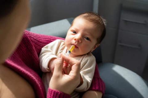 Supported awake newborn receives golden colostrum from an oral syringe