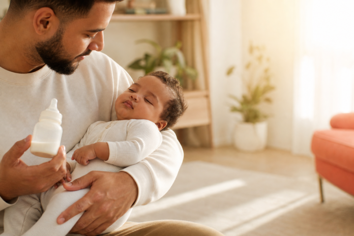 Father holds a sleeping baby beside an untouched bottle