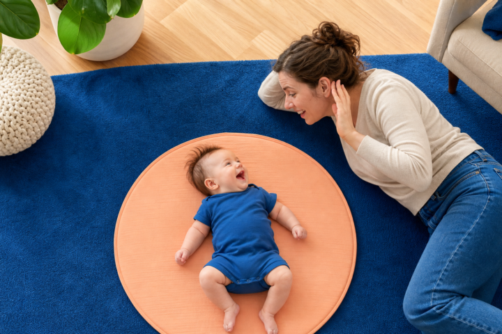 Parent listens as smiling baby vocalizes on a peach play mat