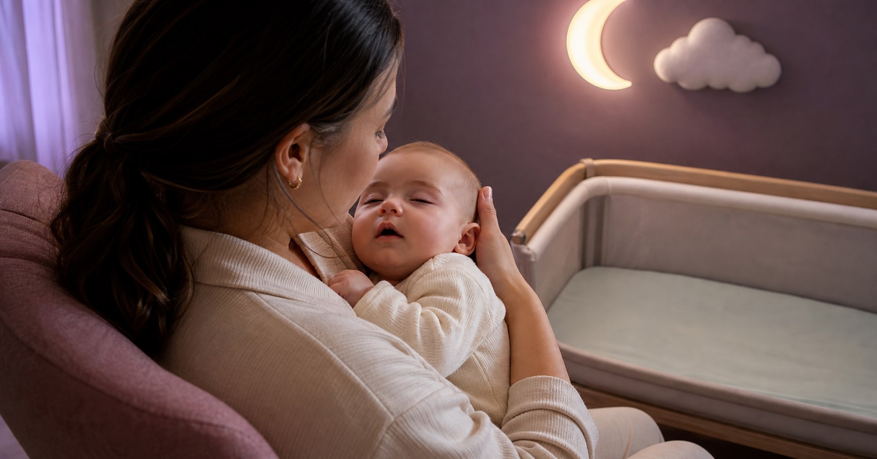 A mother supports a drowsy baby whose eyelids are nearly closed during a calm bedtime cuddle beside an empty bassinet.