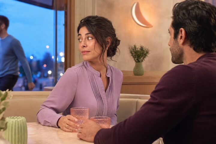 Wife glances toward a man passing the café window while her husband watches her across the table.