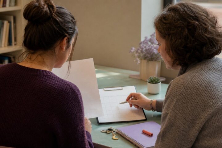 College student and trusted mentor reviewing an unmarked paper and blank rubric grid in a library