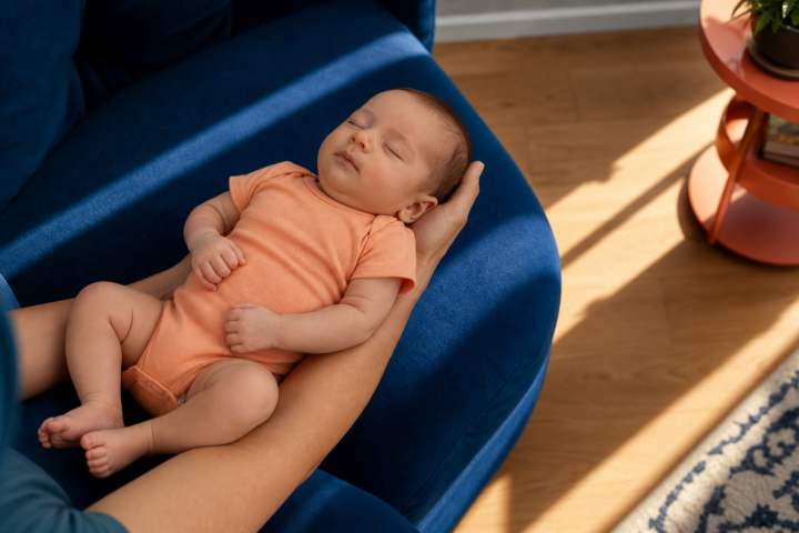 Sleeping baby in a peach onesie cradled on a cobalt chair