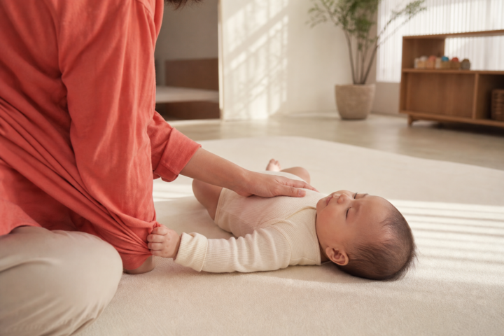 Sleeping baby grips a caregiver's coral shirt on a cream play mat.