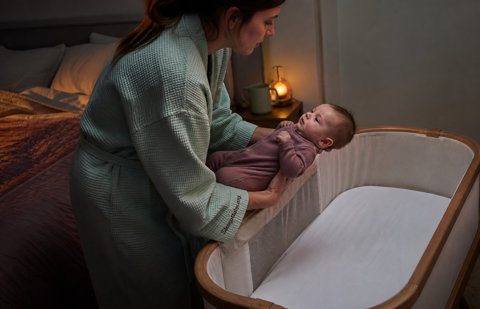 Awake caregiver supports a sleepy ten-week-old above an empty bassinet during a dim evening handoff
